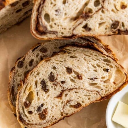 A cinnamon raisin sourdough loaf sliced on brown parchment paper.