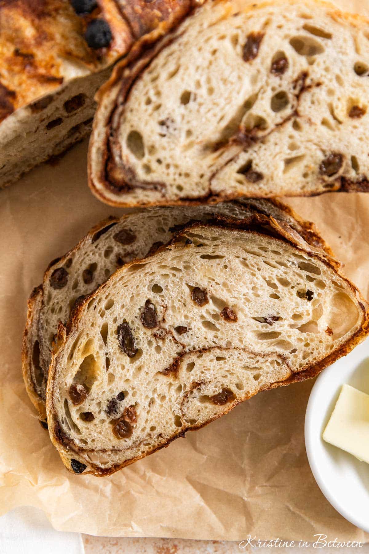 A cinnamon raisin sourdough loaf sliced on brown parchment paper.